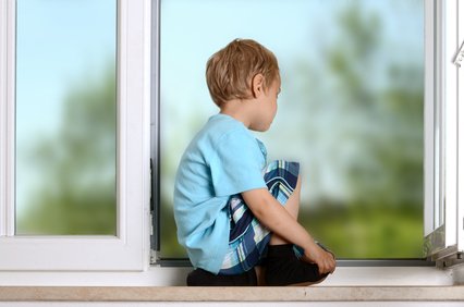 kluk sedí na parapetu a kouká z okna