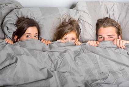 žena, dítě a muž vykukují zpod peřiny v posteli