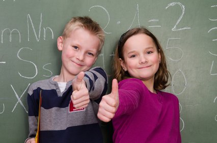 dvě usmívající se děti před školní tabulí