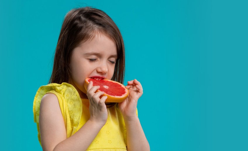 Malá dívka se zakusuje do grapefruitu Malá dívka se zakusuje do grapefruitu