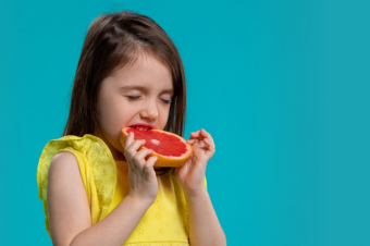 Malá dívka se zakusuje do grapefruitu