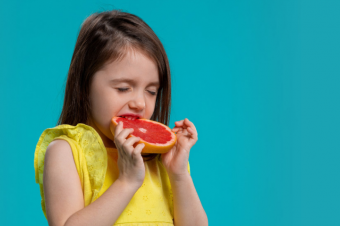 Malá dívka se zakusuje do grapefruitu Malá dívka se zakusuje do grapefruitu