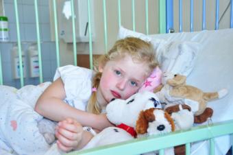 Dívka a plyšák v klecovém lůžku v nemocnici