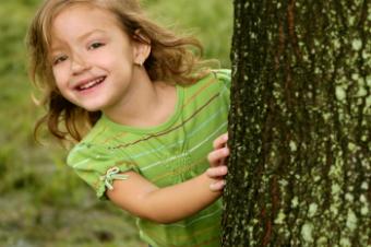Dívka vykukující zpoza stromu