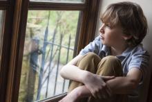 Smutný chlapec se dívá z okna