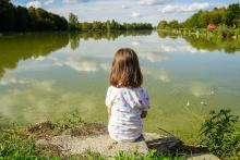 Dívka sedí na břehu rybníka