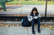 Dívka sedí na obrubníku u školy