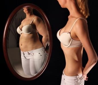 Vyhublá dívka se vidí v zrcadle jako při těle