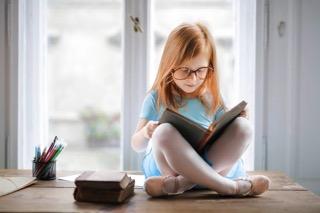 Malá dívka sedí na okně a čte si knihu Malá dívka sedí na okně a čte si knihu