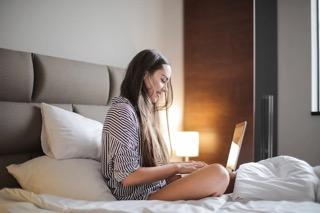 Dívka sedí na posteli a pracuje na počítači Dívka sedí na posteli a pracuje na počítači
