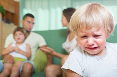 Plačící chlapec se sourozencem a rodiči v pozadí